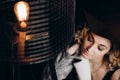 Beautiful elegant blonde girl in a hat on a dark background next to a lamp in the loft style. Soft focus Royalty Free Stock Photo