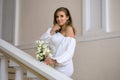 A beautiful elegant bride in a white wedding dress with a bouquet of white flowers is standing indoors Royalty Free Stock Photo