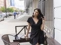 Beautiful elegant brunette girl wearing a black dress with a sexy deep neckline is relaxing in a street cafe. Advertising, fashion Royalty Free Stock Photo