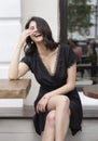 Beautiful elegant brunette girl wearing a black dress with a sexy deep neckline is relaxing in a street cafe. Advertising, fashion Royalty Free Stock Photo