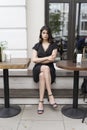 Beautiful elegant brunette girl wearing a black dress with a sexy deep neckline is relaxing in a street cafe. Advertising, fashion Royalty Free Stock Photo