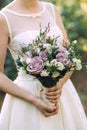 Beautiful elegant summer wedding bouquet of lilac roses and wildflowers in the hands of the bride in white wedding dress Royalty Free Stock Photo