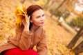 Beautiful elegant woman in autumn park holds an autumn yellow leaves near the face. Young woman in a beige coat walks Royalty Free Stock Photo