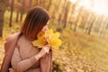 Beautiful elegant woman in autumn park holds an autumn yellow leaves near the face. Young woman in a beige coat walks Royalty Free Stock Photo