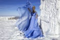 Beautiful elegant woman wearing blue fluttering long dress and is posing on a sunny day in the mountains. Snow queen Royalty Free Stock Photo