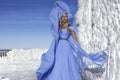 Beautiful elegant woman wearing blue fluttering long dress and is posing on a sunny day in the mountains. Snow queen