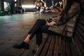 Beautiful elegant women& x27;s legs in black glossy loafers. A woman sits on a bench on a night street in the city in autumn