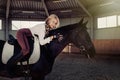 Beautiful elegant young blonde girl lies on a her black horse dressing uniform competition white blouse shirt and brown pants. Royalty Free Stock Photo