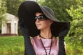 Beautiful elegant young lady enjoying a day in the park. Big black hat and sunglasses. Royalty Free Stock Photo