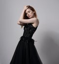 Beautiful elegant young model with bright foxy hairstyle posing in fashion chic black dress with long skirt on studio grey