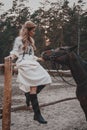 Beautiful and elegant young woman wearing the dress is stroking the horse on the ranch Royalty Free Stock Photo