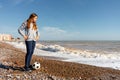 A beautiful emotional girl in a gray sweatshirt posing with her soccer ball while looking at the horizon on a pebble Royalty Free Stock Photo