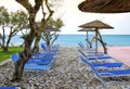 Beautiful empty beach with rows of sun beds under straw umbrellas and trees. Zakinthos, Greece