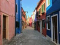 A beautiful empty narrow shaded cobblestone street with an array of old colourful square homes on the small island of Burano