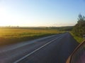 Beautiful empty road beside the sunlit grassy meadow. Royalty Free Stock Photo