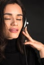 Beautiful enjoying young woman listening the music in wireless headphone with closed eyes on dark black background