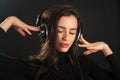 Beautiful enjoying young woman listening the music in wireless headphone with closed eyes on dark black background