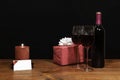 Beautiful etched wine glasses and bottle of red wine, red candle, wrapped present with bow on wooden table with name tag on dark