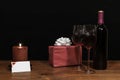 Beautiful etched wine glasses and bottle of red wine, red candle, wrapped present with bow on wooden table with name tag on dark