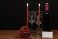 Beautiful etched wine glasses and bottle of red wine, red candles and red roses on wooden table with name tag on dark background