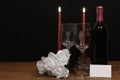 Beautiful etched wine glasses and bottle of red wine, red candles and white roses on wooden table with name tag on dark background Royalty Free Stock Photo