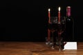 Beautiful etched wine glasses and bottle of red wine, lighted by red candles, on wooden table with name tag on dark background