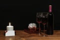Beautiful etched wine glasses and bottle of red wine, white candle, wrapped present with bow on wooden table with name tag on dark