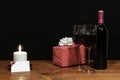 Beautiful etched wine glasses and bottle of red wine, white candle, wrapped present with bow on wooden table with name tag on dark