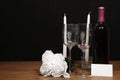 Beautiful etched wine glasses and bottle of red wine, white candles and white roses on wooden table with name tag on dark