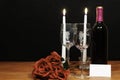 Beautiful etched wine glasses and bottle of red wine, white candles and red roses on wooden table with name tag on dark background