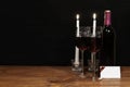 Beautiful etched wine glasses and bottle of red wine, white candles, on wooden table with name tag on dark background