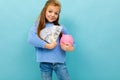 Beautiful european girl holding a piggy bank and money in hands on a light blue wall Royalty Free Stock Photo