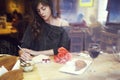 Beautiful european woman with long hair writing in notebook near window in cafe. Romantic breakfast, date or St. Valentine`s Day.