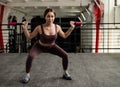 A beautiful European woman squats with a bar on her shoulders. Young girl in sportswear doing exercises on buttock Royalty Free Stock Photo