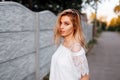 Beautiful european young blond woman in a white lace elegant blouse is resting outdoors at sunset. Happy attractive girl model Royalty Free Stock Photo