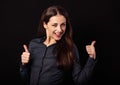 Beautiful excited energetic smiling business woman showing fingers thumb up, the ok sign in blue shirt on black background. Royalty Free Stock Photo