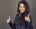 Beautiful excited energetic smiling business woman showing fingers thumb up by two hands, the ok sign in blue shirt on grey Royalty Free Stock Photo