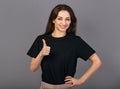 Beautiful excited energetic smiling casual woman showing finger thumb up by hand, the ok sign in blacl shirt on grey light studio Royalty Free Stock Photo