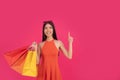 Beautiful excited happy asian woman posing isolated over pink wall background holding shopping bags pointing up, free spase for