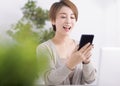 Beautiful excited young woman watching mobile phone in living room