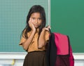 Beautiful and exotic looking female child in school uniform carrying student bag smiling in front of classroom blackboard in back