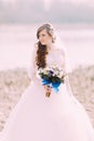 Beautiful fabulous curly bride with stylish bouquet standing on the beach.