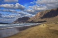 Beautiful Famara Beach, Lanzarote, Spain. Mountains in the background. A woman walking along the sandy beach. A blue sky with some