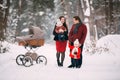 A beautiful family with retro pram walks through the winter snowy forest