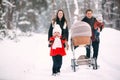 A beautiful family with retro pram walks through the winter snowy forest