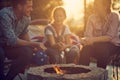 Beautiful family of three roasting marshmallows together by a fireplace, sitting in cozy chairs outdoors