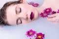 Beautiful fashion model girl taking a milk bath with flowers, advertisement of a skincare product. Royalty Free Stock Photo