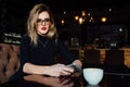 Beautiful fashionable stylish girl sits in a cafe with a cup of coffee. Royalty Free Stock Photo