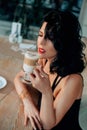 Beautiful fashion woman sitting in street cafe, enjoy aroma taste coffee. Closeup portrait brunette lady with long curls Royalty Free Stock Photo