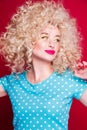 Beautiful fashionable blonde girl in retro style with voluminous curly hairstyle, in a blue polka dot blouse on a red background Royalty Free Stock Photo